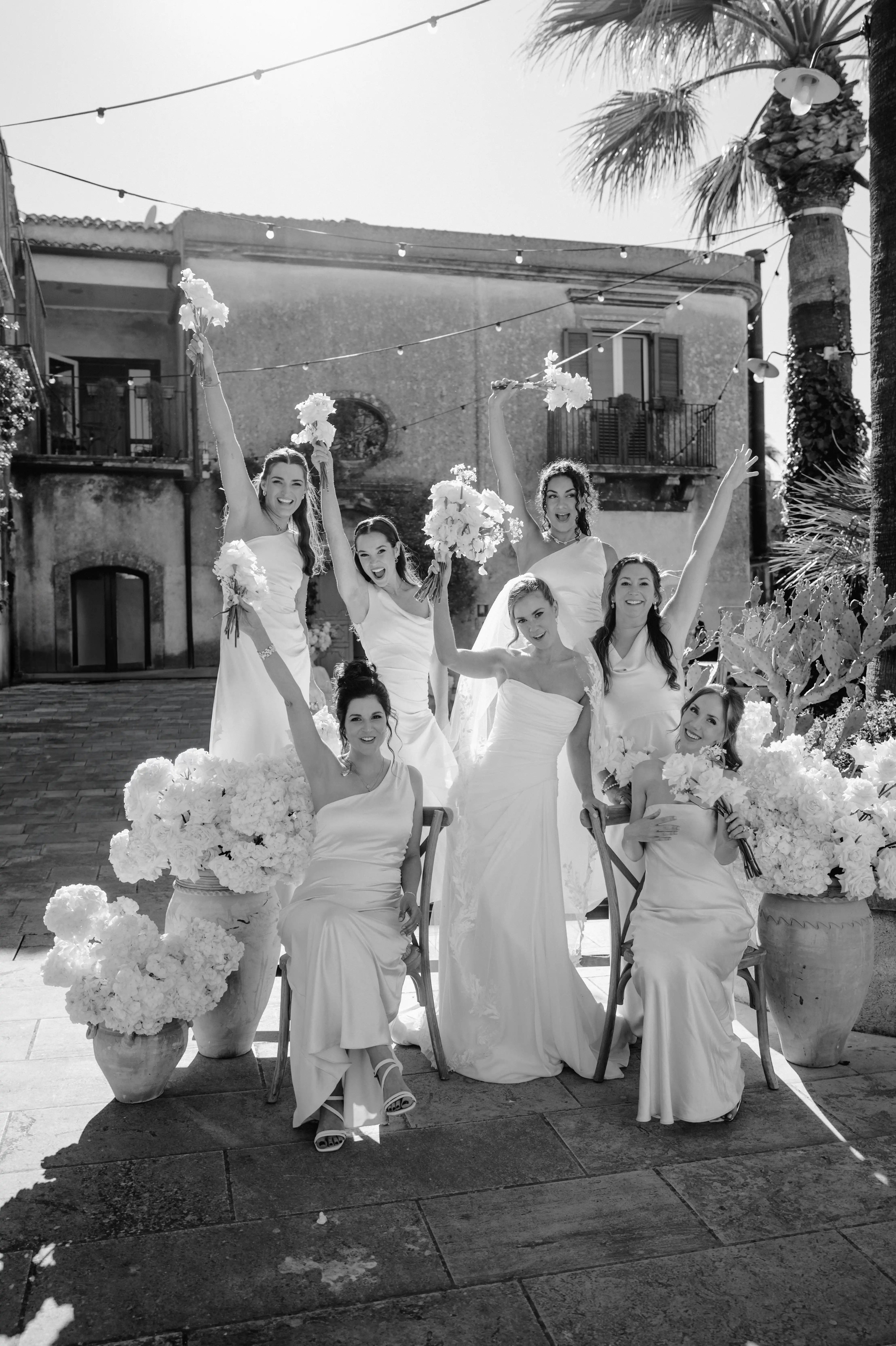 Black and white bridal party portrait with bridesmaids celebrating in a historic Sicilian courtyard.